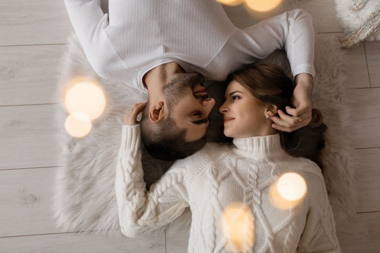 Couple lying on a carpet holding each other's heads and gazing lovingly, symbolizing emotional connection and intimacy